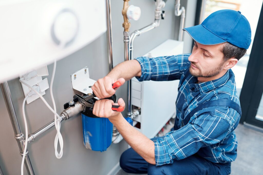 Plumber using pliers on pipe fittings beside a water filter housing
